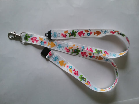 Lanyard made with white ribbon with lots of fish as the pattern it has a safety breakaway lanyard id or whistle holder